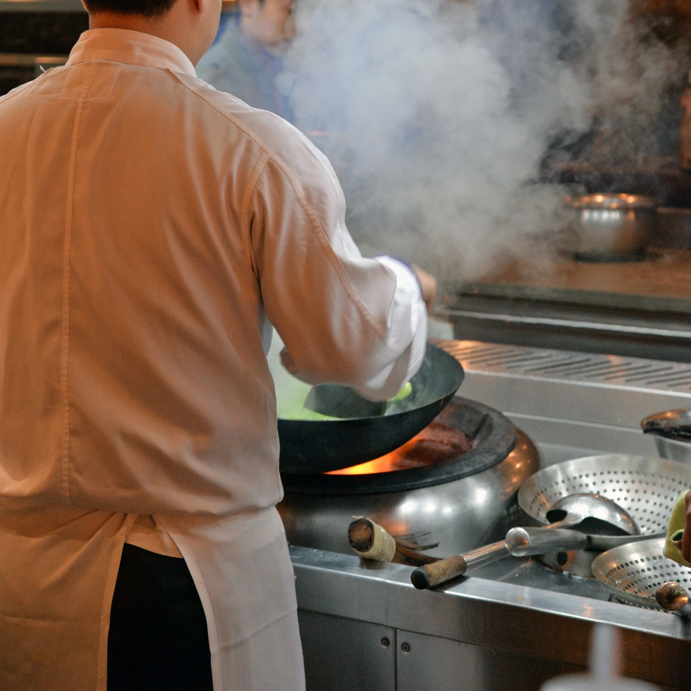 Chef cooking over a wok in a professional Chinese restaurant kitchen
