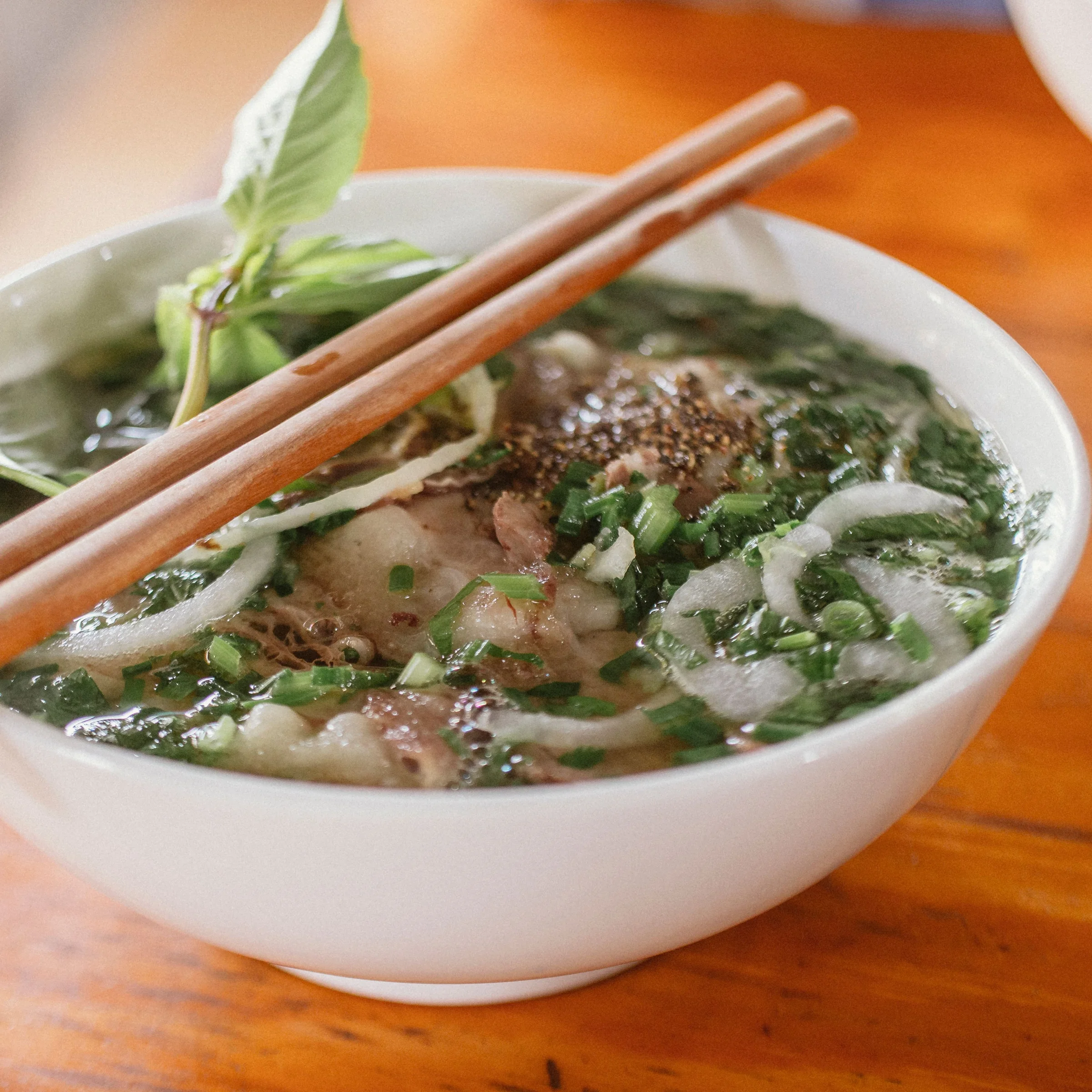 Bowl of Vietnamese pho with fresh herbs, onion, and chopsticks