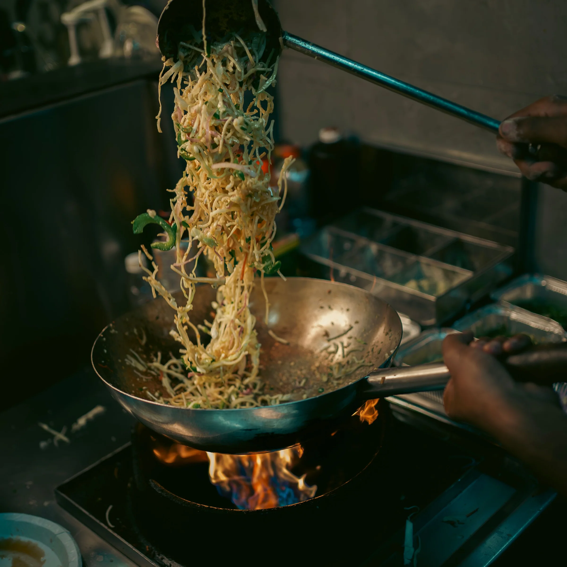 Chef tossing stir-fried noodles in a flaming wok