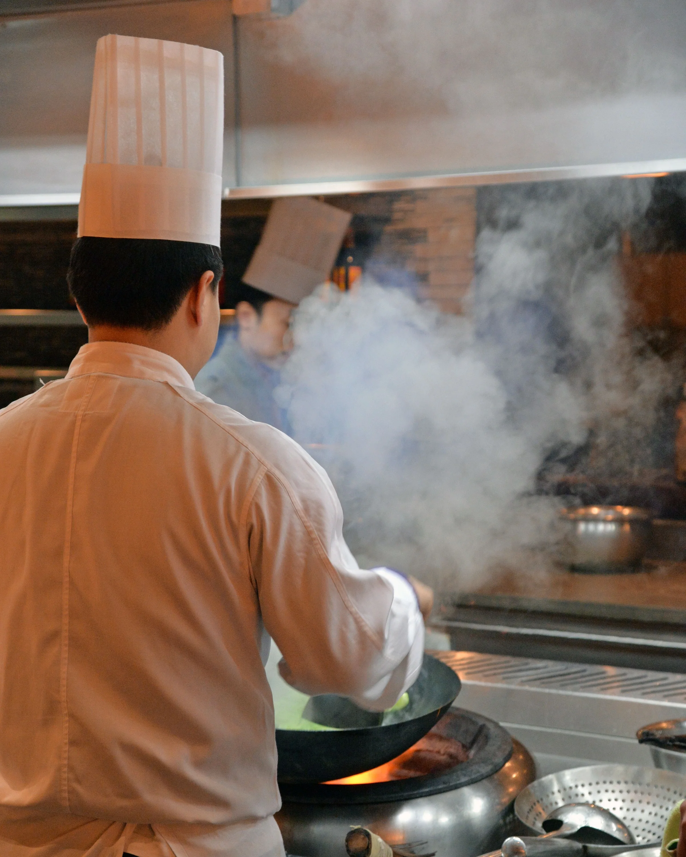 Chef stir-frying over an open flame wok in a professional Chinese restaurant kitchen